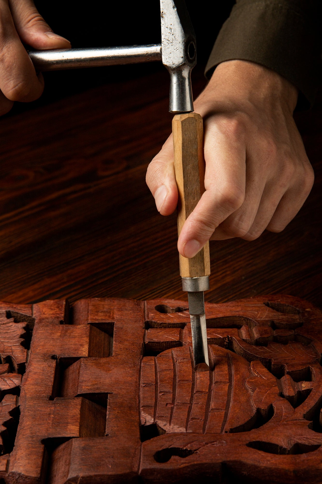 Hands carving wood with a chisel and hammer